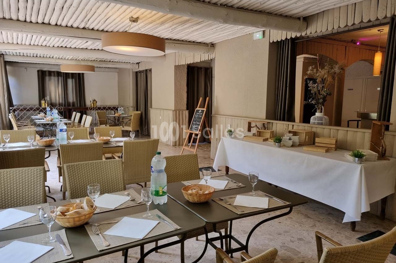 Salle de restaurant lumineuse avec tables dressées, chaises en osier, buffet décoré et ambiance sobre.