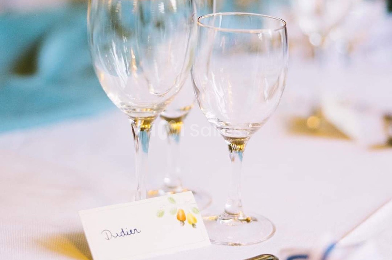 Trois verres à pied vides posés sur une table blanche avec une carte de place portant un prénom.