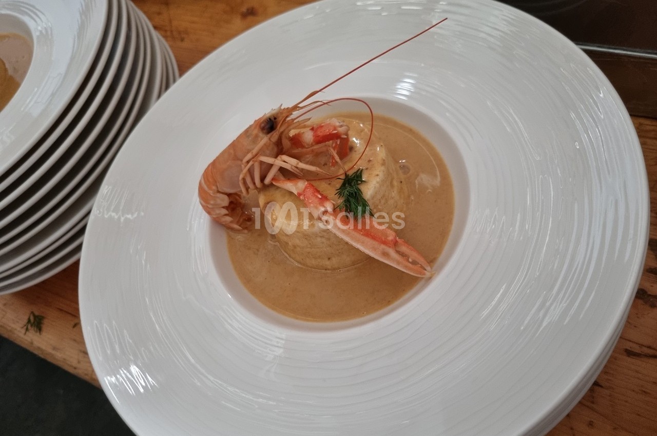 Assiette de bisque de crustacés avec une langoustine entière et une garniture d'aneth, servie sur une table en bois.