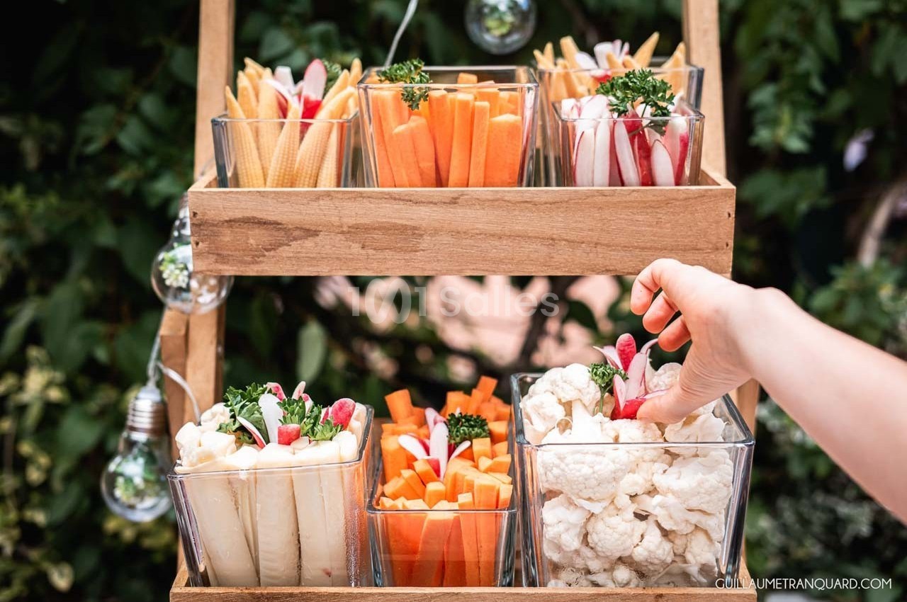 Plateau en bois avec des verrines contenant des légumes crus variés, une main prenant un radis.
