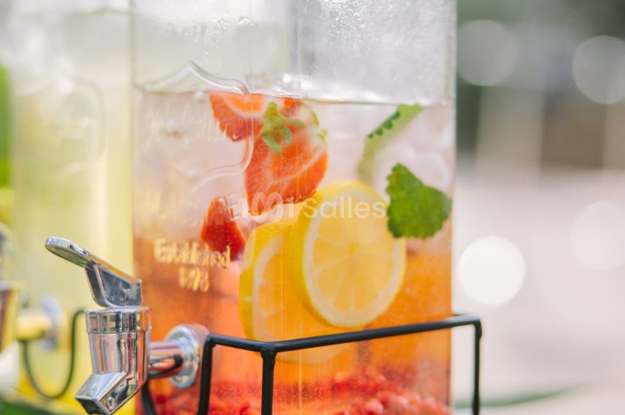 Distributeur de boisson contenant une infusion d'eau avec des tranches de citron, fraises et feuilles de menthe.