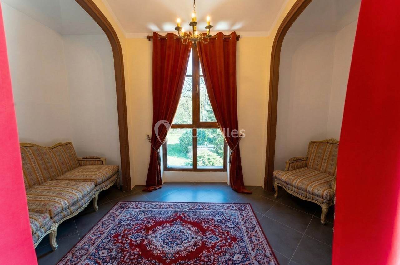 Deux canapés classiques encadrent une fenêtre avec rideaux rouges, éclairée par un lustre, sur un tapis oriental.