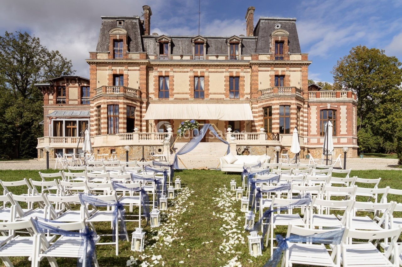 Chaises blanches alignées en extérieur devant un château, avec une arche décorée pour une cérémonie.