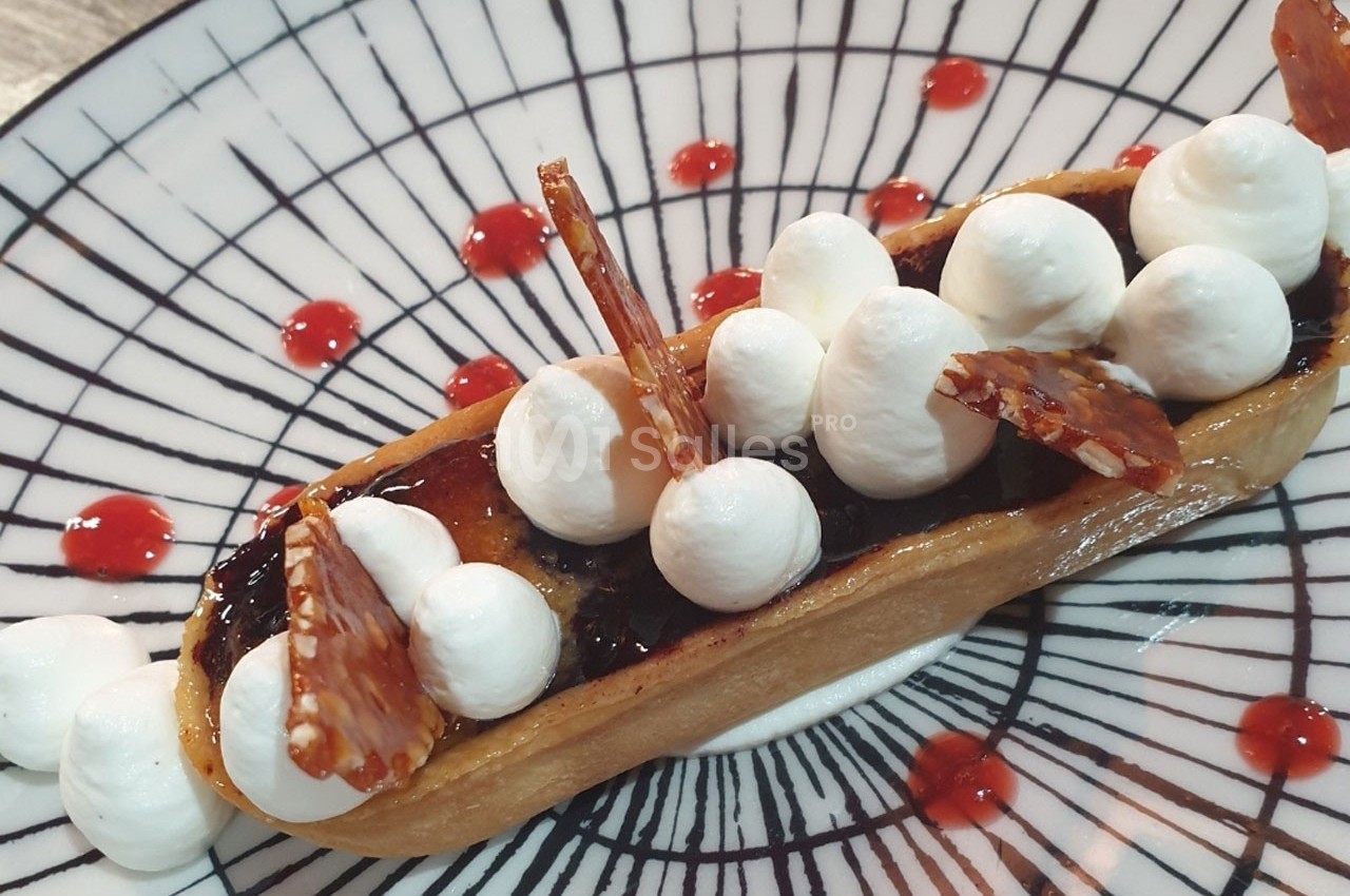 Tartelette garnie de crème chantilly, caramel croquant et coulis rouge sur une assiette décorée.
