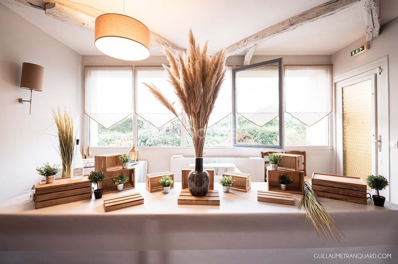 Table décorée avec des éléments naturels, comprenant des plantes, des pampas et des caisses en bois, dans une pièce…