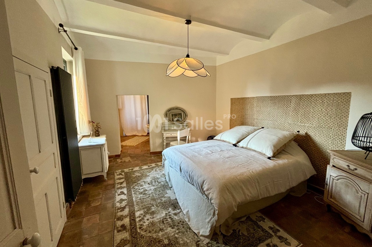 Chambre lumineuse avec lit double, mobilier en bois clair, tapis au sol et lampe suspendue au plafond.