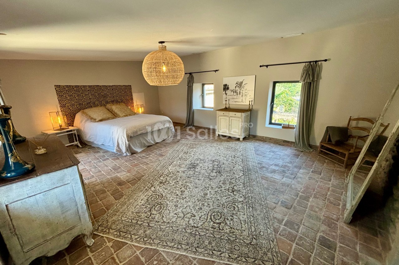 Chambre spacieuse avec lit double, tapis central, mobilier en bois clair et lumière naturelle provenant des fenêtres.