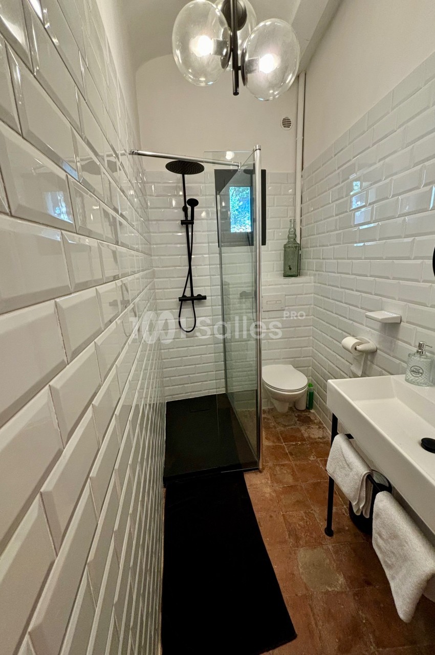 Salle de bain étroite avec douche à l'italienne, carrelage blanc, sol en terre cuite et lavabo avec miroir rond.