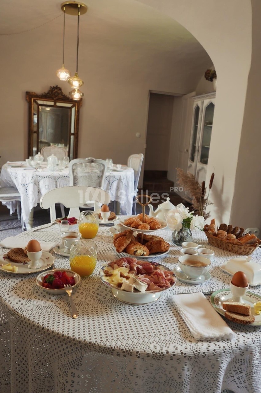 Table dressée pour un petit-déjeuner avec viennoiseries, fruits, œufs, jus d'orange et café dans une salle élégante.