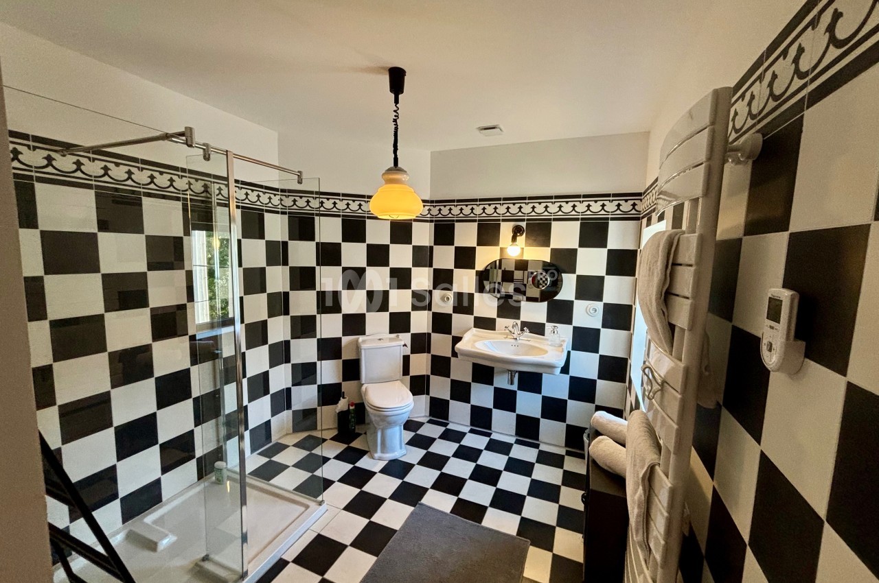 Salle de bain avec carrelage noir et blanc, douche vitrée, lavabo, toilettes et éclairage suspendu.