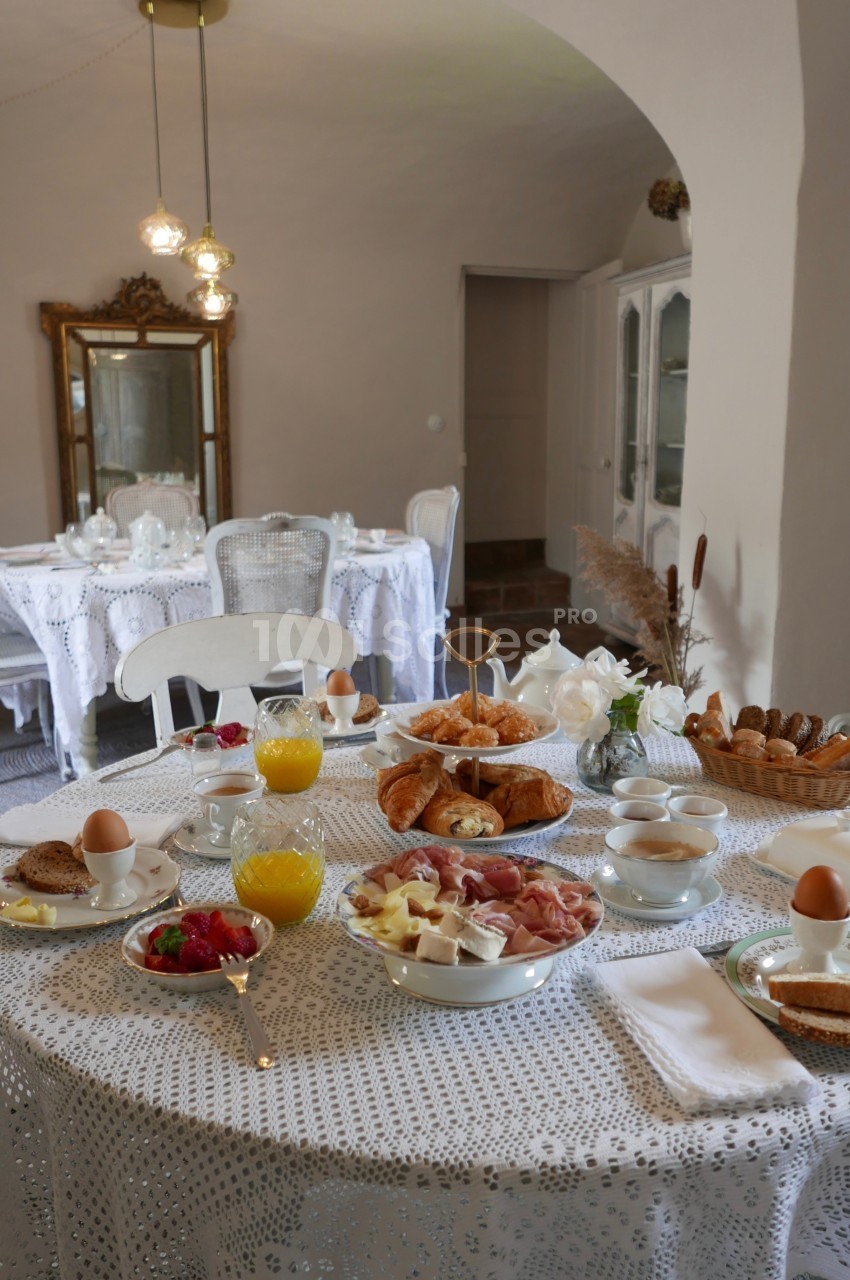 Table dressée pour un petit-déjeuner avec viennoiseries, fruits, œufs, jus d'orange et vaisselle élégante dans une salle…