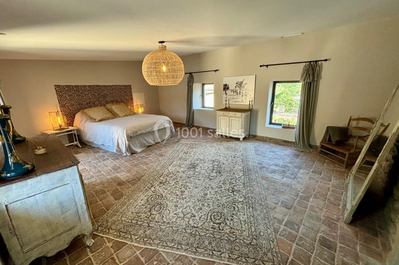 Chambre spacieuse avec lit double, tapis central, mobilier en bois clair et lumière naturelle provenant des fenêtres.