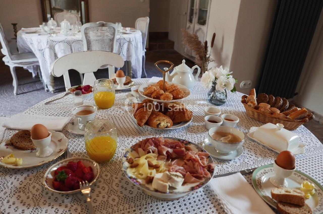 Table dressée pour un petit-déjeuner avec viennoiseries, fruits, charcuterie, œufs, pain, jus d'orange et thé.