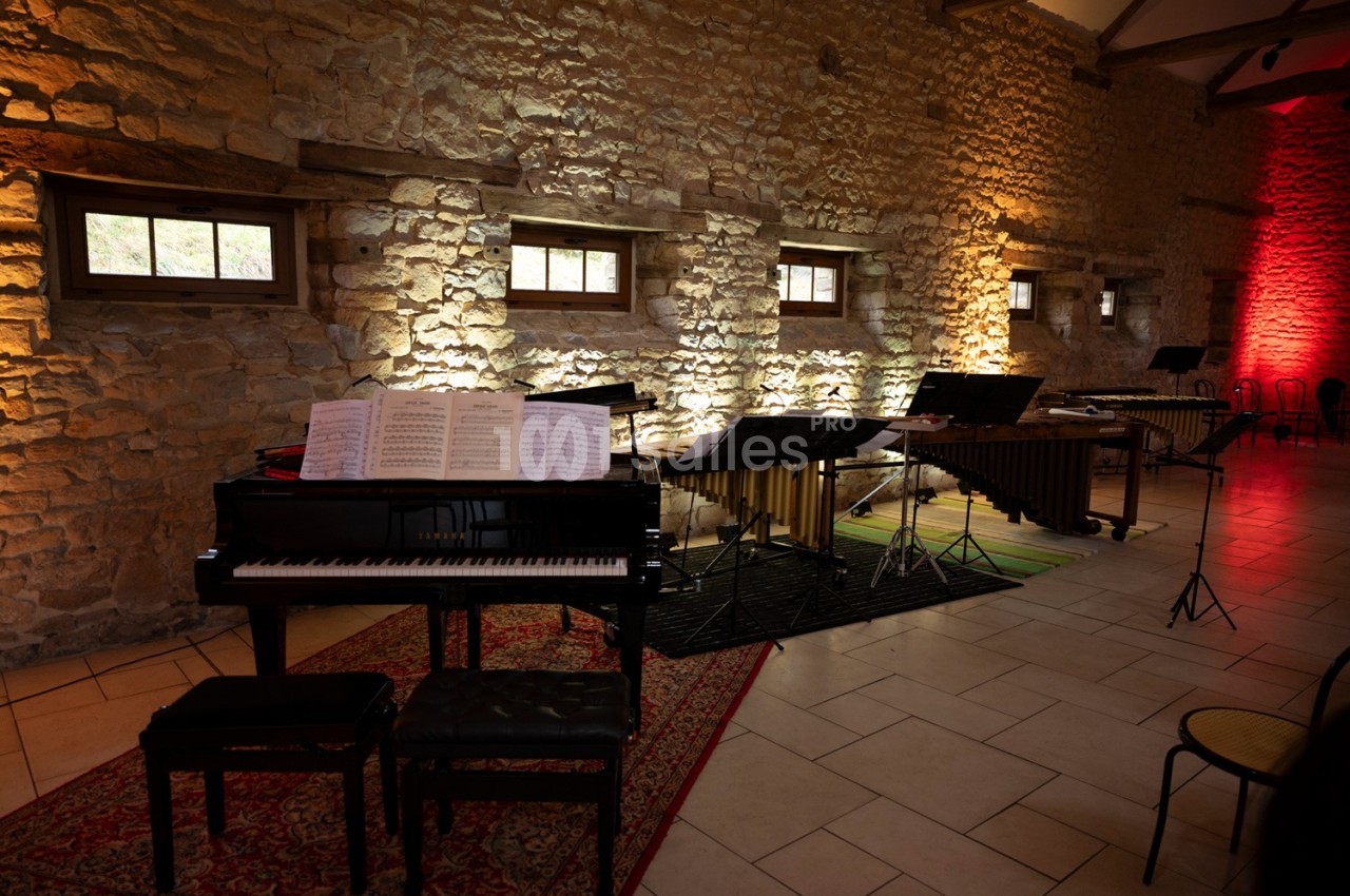 Salle en pierre éclairée, avec un piano à queue, des partitions ouvertes et des instruments de percussion disposés.