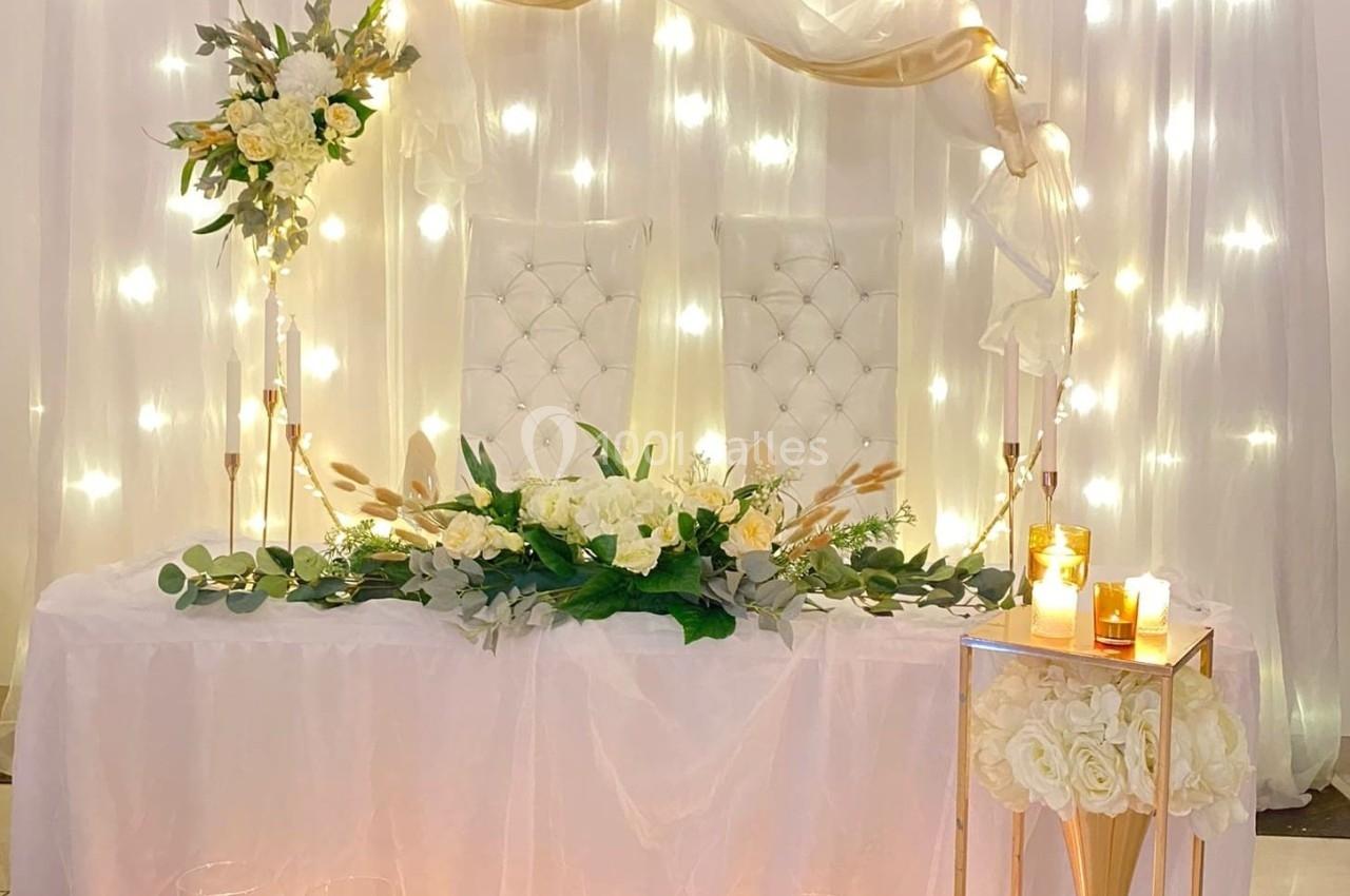 Décoration de table de mariage avec fleurs blanches, bougies allumées et rideau lumineux en arrière-plan.