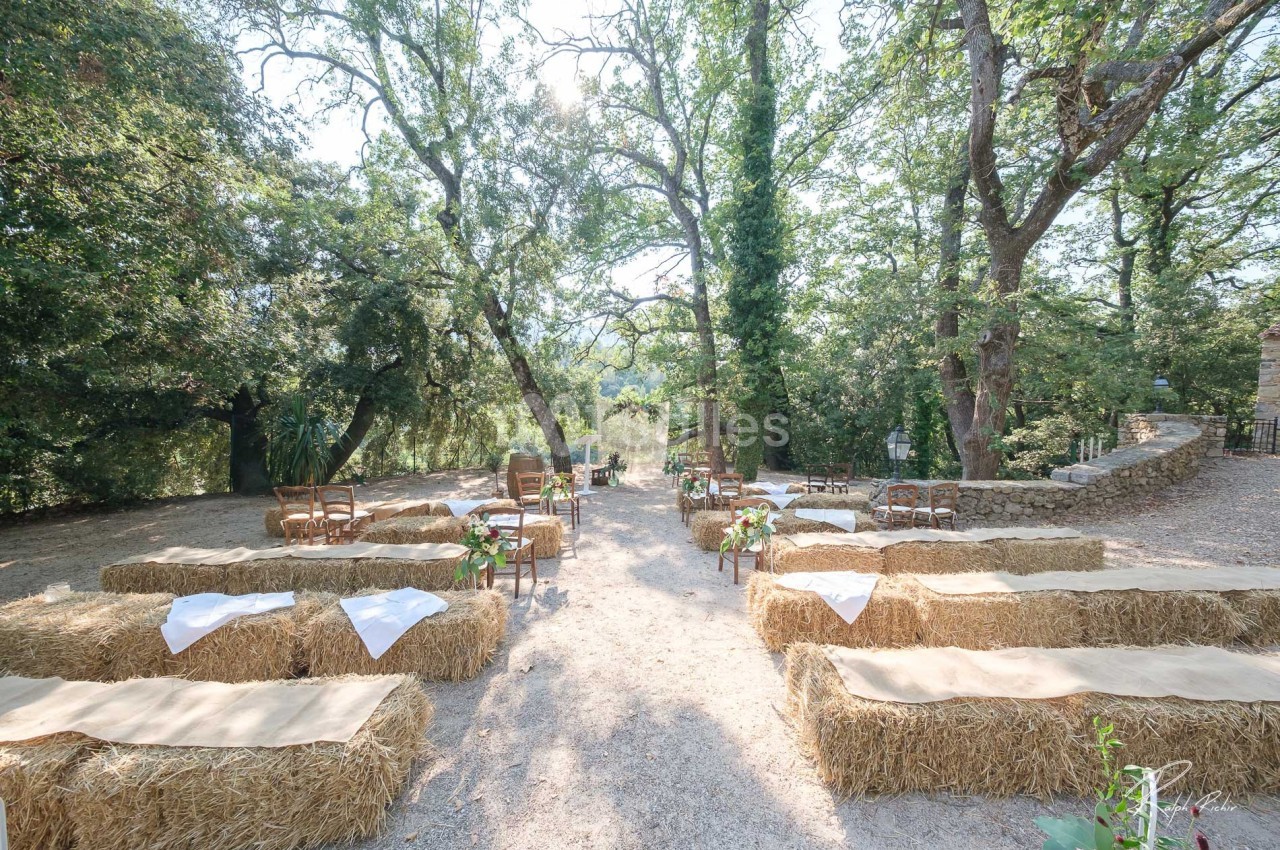 Disposition de bottes de paille et chaises en extérieur sous des arbres, formant un espace pour une cérémonie en plein air.