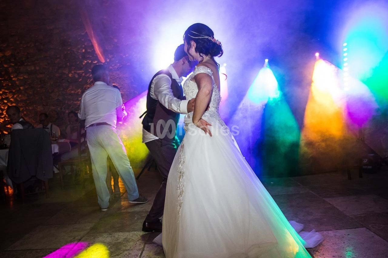 Un couple danse lors d'une soirée festive, éclairée par des lumières colorées et une ambiance animée.
