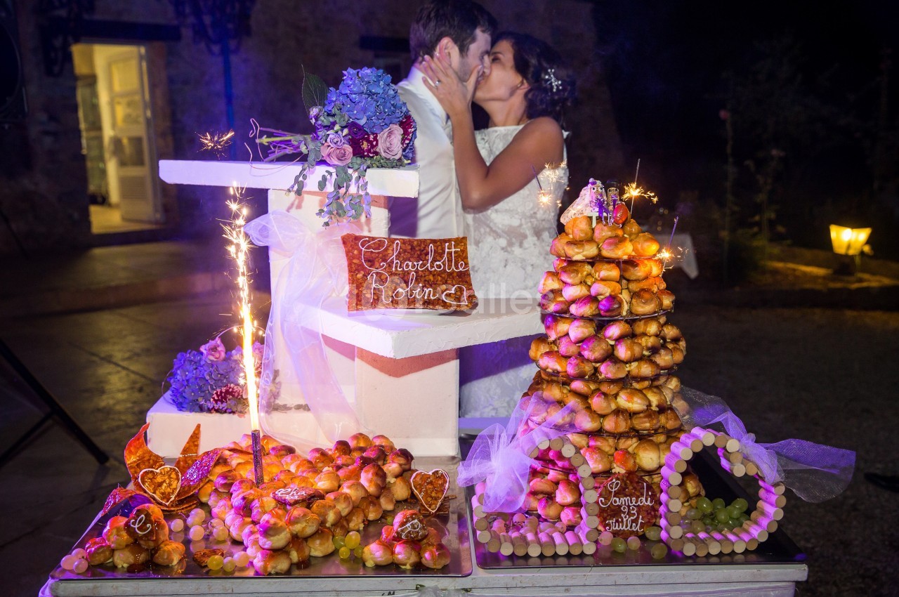 Un couple de mariés s'embrasse devant une pièce montée et des desserts décorés lors d'une réception nocturne.