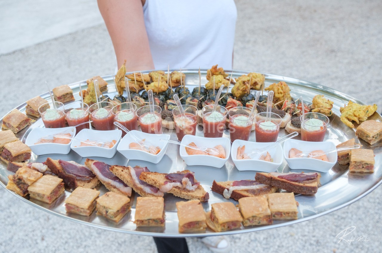 Plateau de canapés variés avec verrines, bouchées salées et amuse-bouches, tenu par une personne en extérieur.