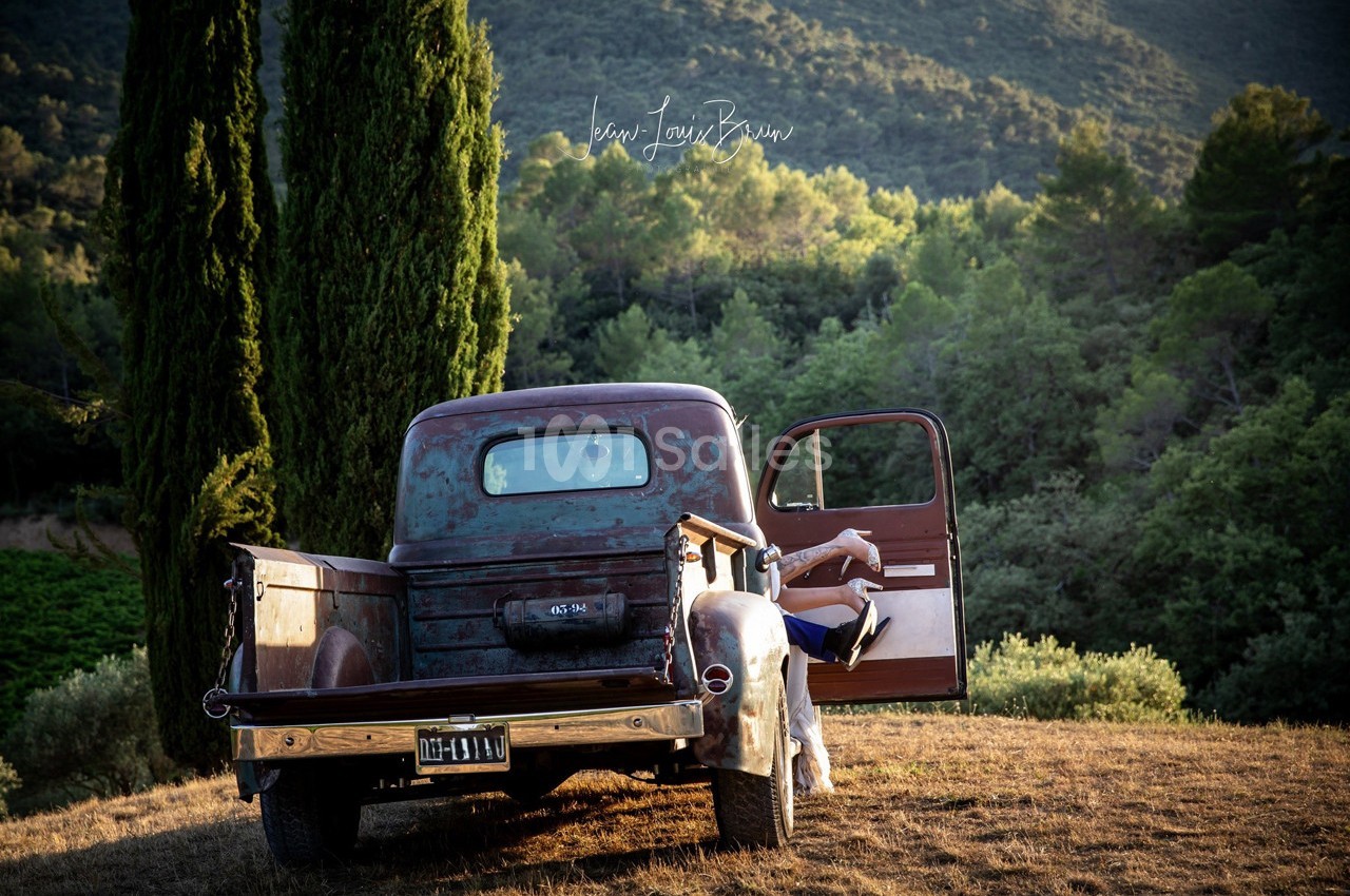 Un vieux pick-up rouillé stationné dans un paysage rural avec une personne assise sur le marchepied, porte ouverte.