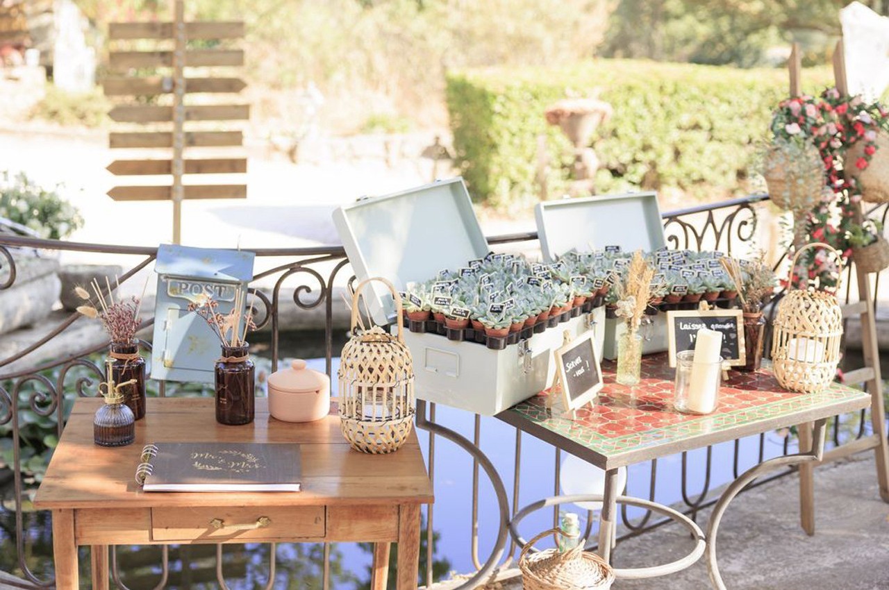 Table décorative en extérieur avec des plantes en pots, un carnet ouvert et des éléments en osier près d'un point d'eau.