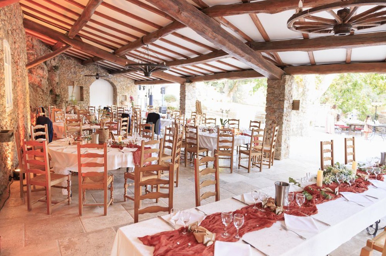 Salle de réception rustique avec tables décorées de nappes blanches et chemins de table rouges, chaises en bois.