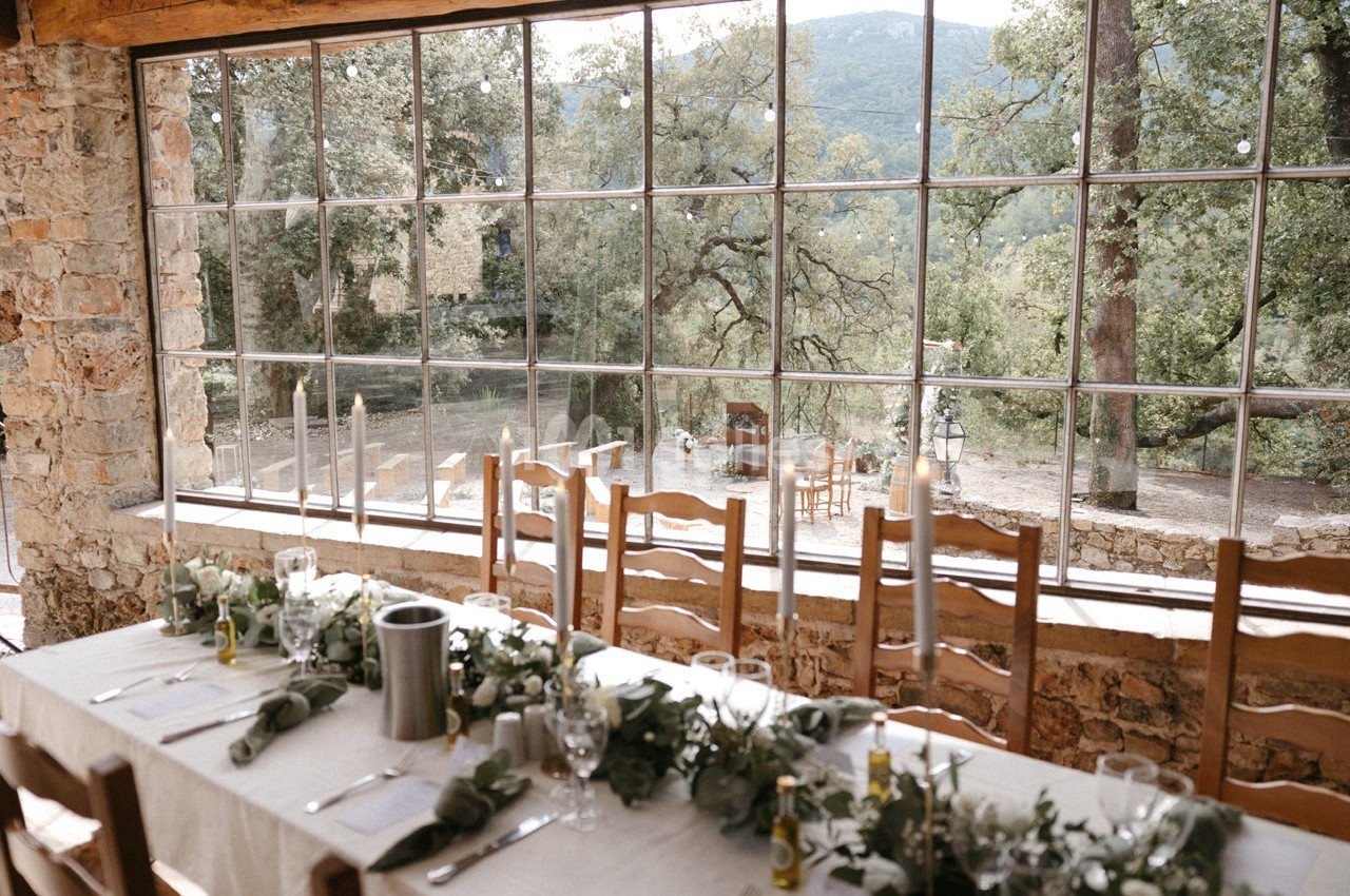Grande table dressée avec des chaises en bois, vue sur un jardin arboré à travers une large baie vitrée.