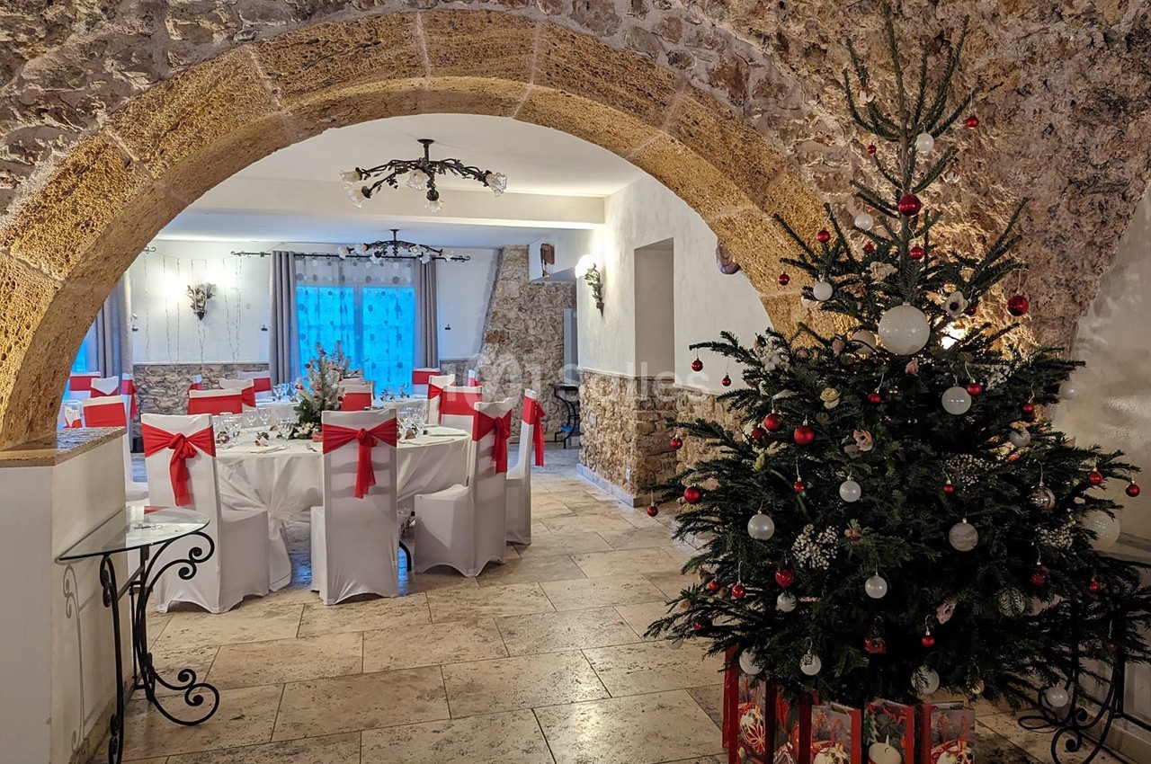 Salle voûtée décorée pour Noël avec un sapin orné de boules rouges et blanches et des tables dressées pour un repas.