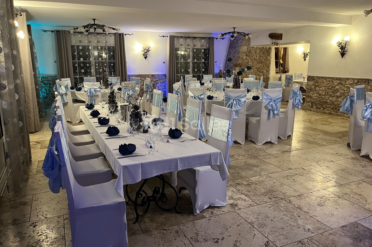 Salle de réception décorée avec des tables dressées, des chaises blanches ornées de nœuds bleus et un éclairage chaleureux.