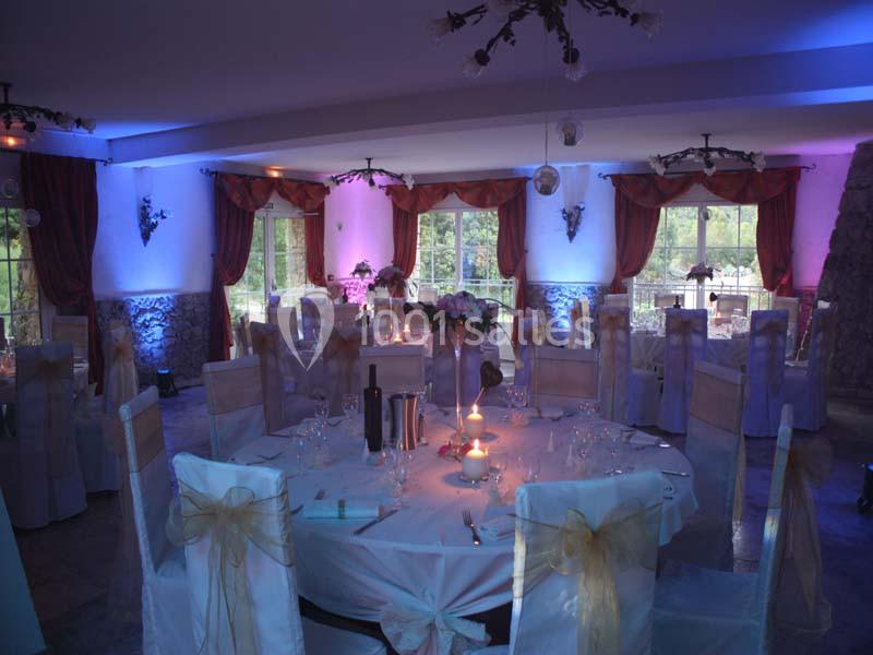 Salle de réception décorée avec des tables rondes, nappes blanches, chaises ornées de nœuds dorés et éclairage tamisé.