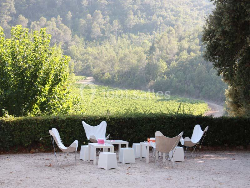 Mobilier de jardin blanc disposé sur une terrasse en gravier, avec vue sur des vignes et une forêt en arrière-plan.
