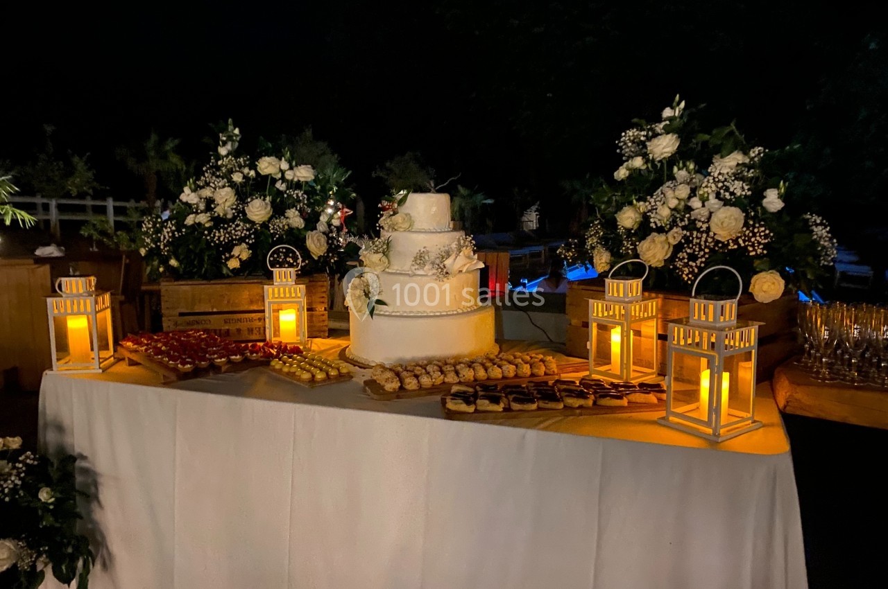 Table décorée pour un mariage avec un gâteau à étages, des lanternes allumées et des fleurs blanches.