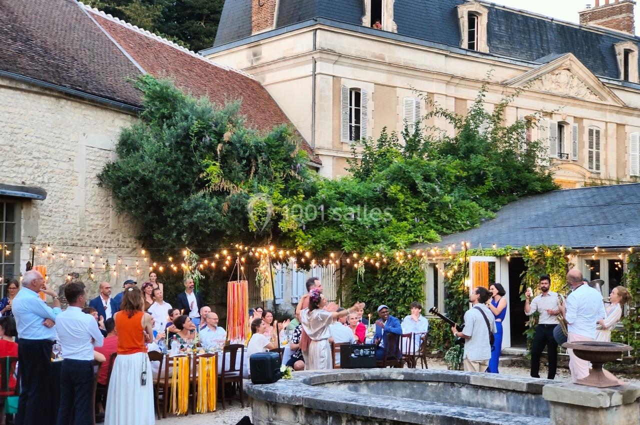 Groupe de personnes réunies dans une cour extérieure décorée de guirlandes lumineuses devant un bâtiment ancien.