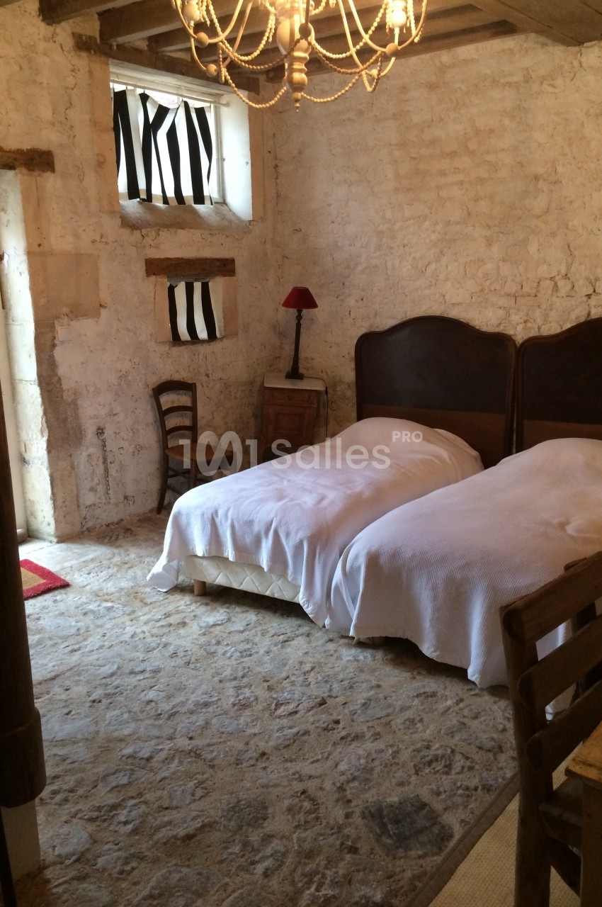 Chambre rustique avec murs en pierre, deux lits simples, un lustre, une lampe rouge et des meubles en bois.