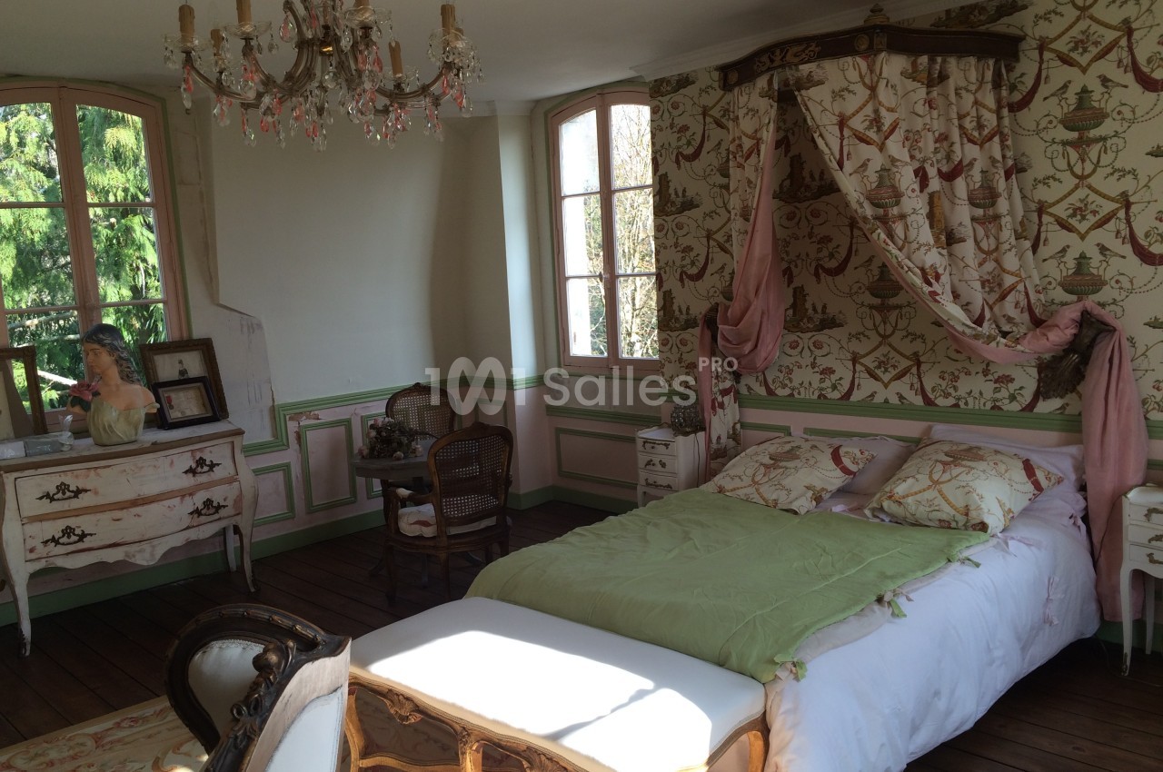 Chambre lumineuse au style ancien avec lit à baldaquin, meubles en bois sculpté et vue sur un jardin verdoyant.