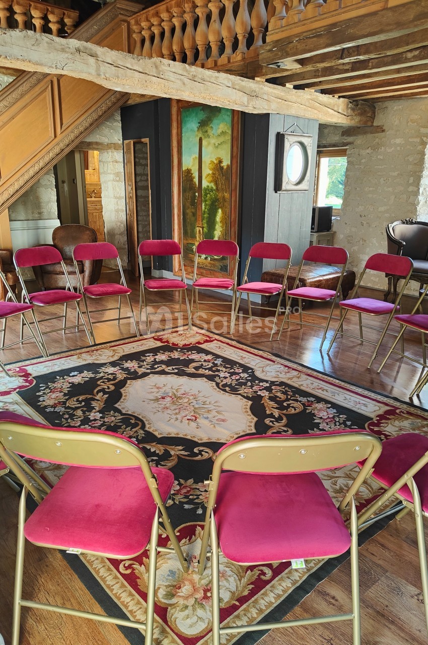 Chaises pliantes rouges disposées en cercle dans une salle rustique avec poutres apparentes et tapis décoratif au sol.