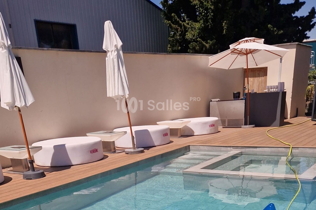 Piscine extérieure avec terrasse en bois, transats blancs, parasols et mur beige en arrière-plan.