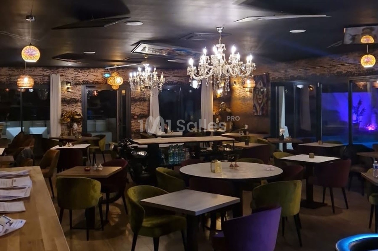 Salle de restaurant élégante avec tables en bois, chaises colorées, lustres et éclairage tamisé.