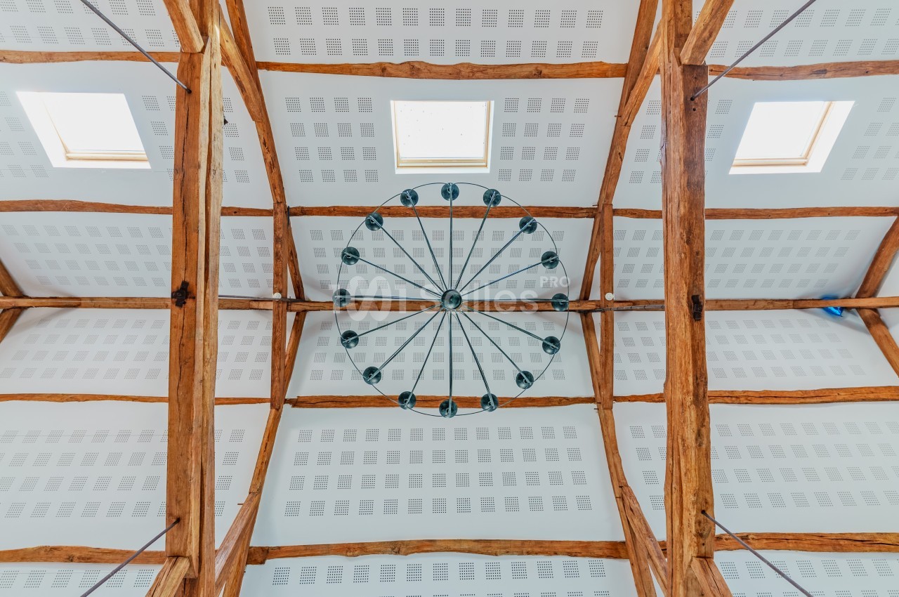 Plafond avec poutres en bois apparentes, lustre circulaire central et panneaux acoustiques blancs.