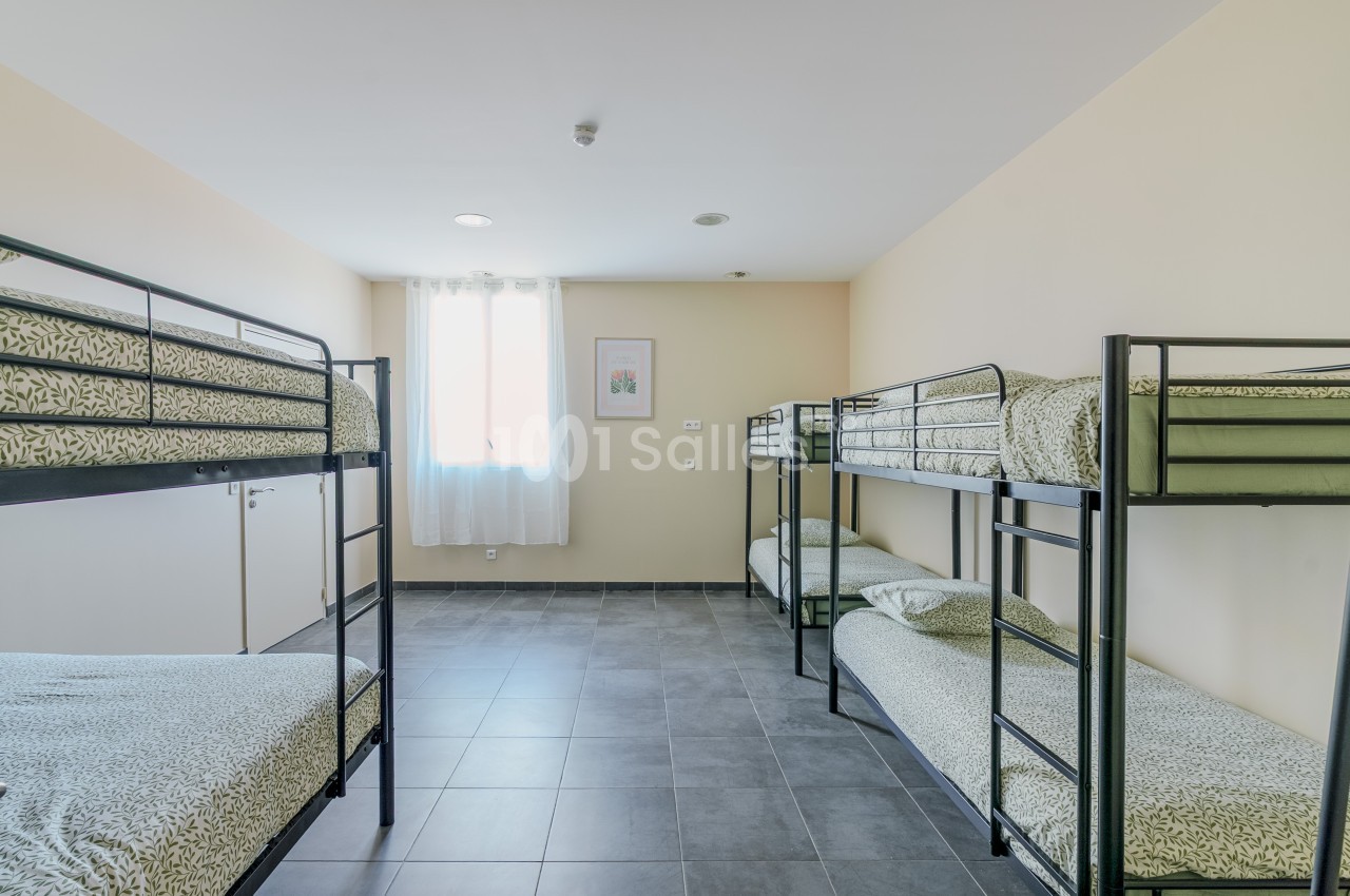 Chambre lumineuse avec quatre lits superposés, draps à motifs verts et sol en carrelage gris.