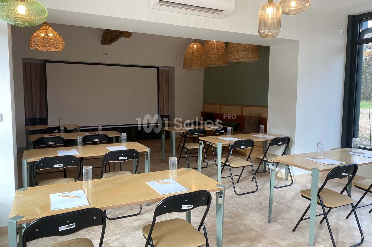 Salle de réunion lumineuse avec tables, chaises pliantes, écran de projection et bouteilles d'eau sur chaque table.