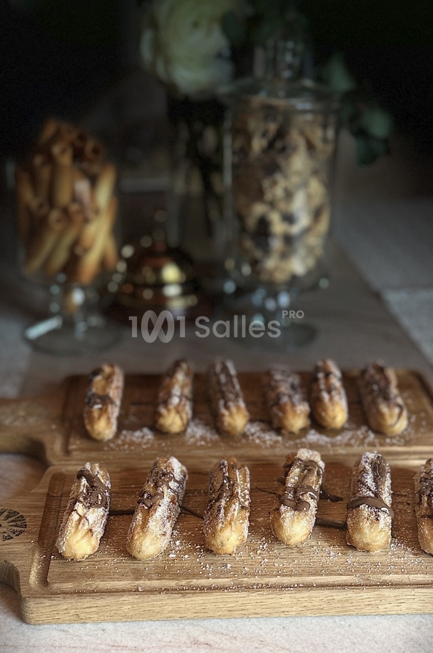 Éclairs au chocolat disposés sur des planches en bois, avec des biscuits et décorations en arrière-plan.