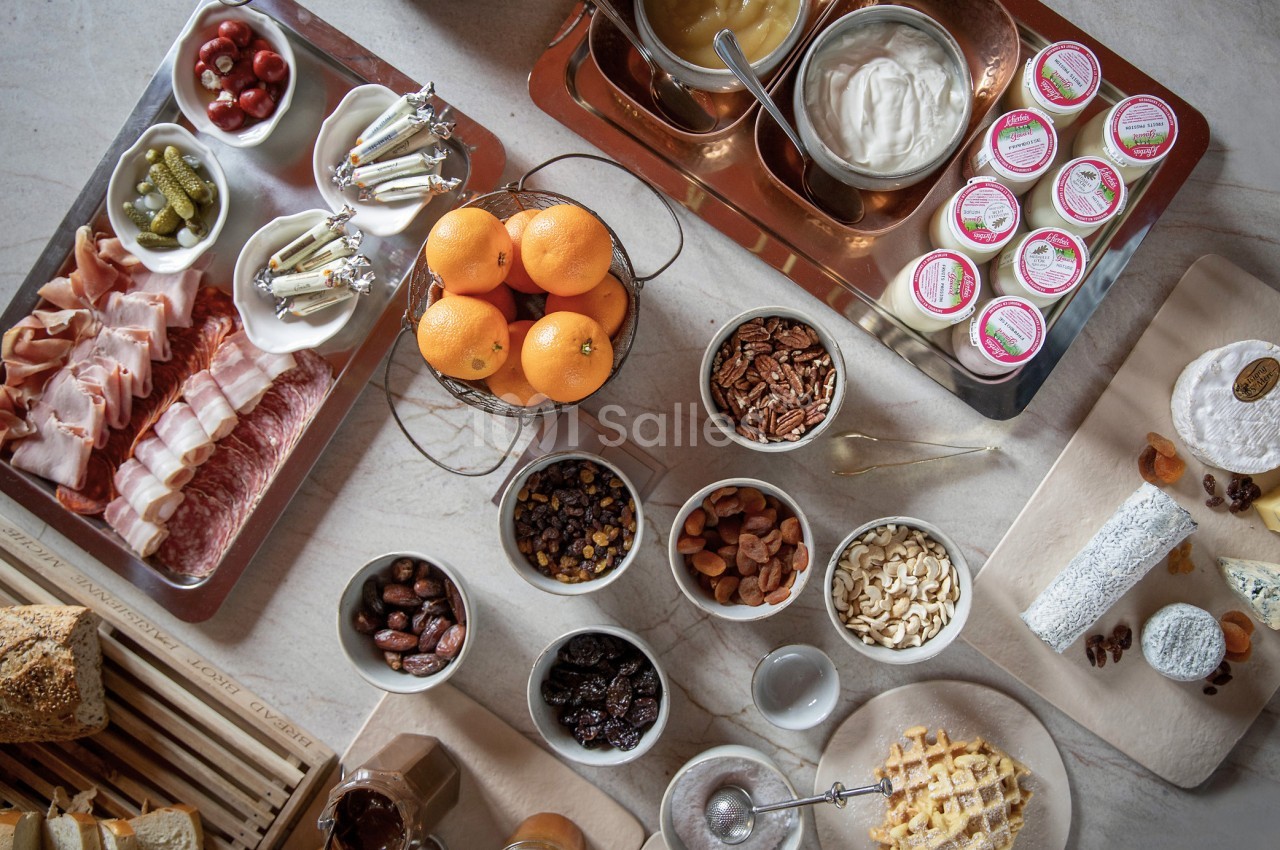 Plateau de petit-déjeuner avec charcuterie, fromages, fruits secs, noix, confitures, miel, oranges et viennoiseries.