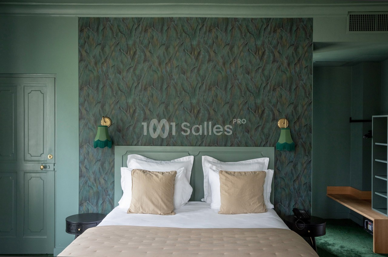 Lit double avec coussins beiges, encadré par des lampes murales vertes, dans une chambre aux tons verts et mur texturé.