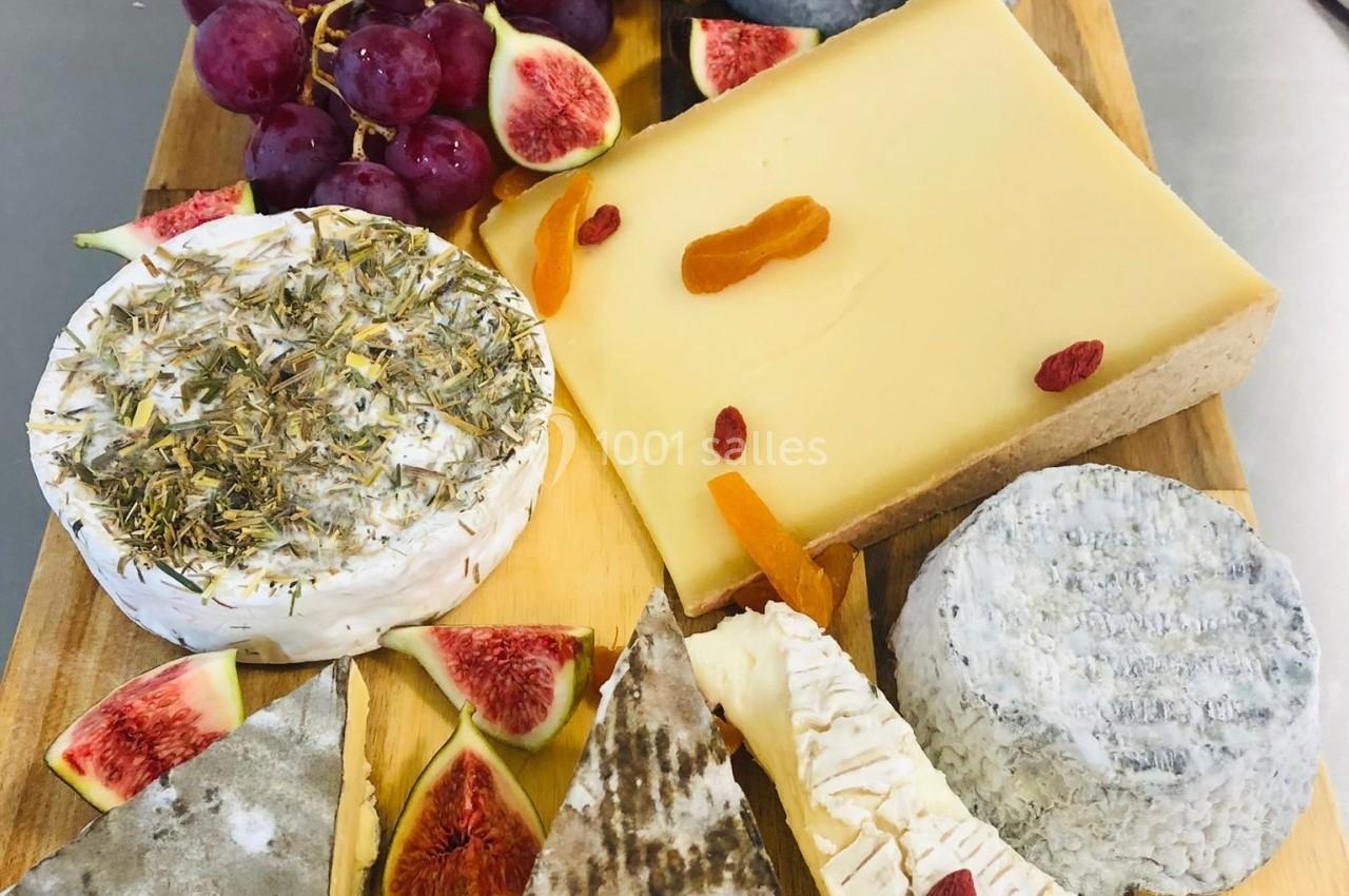 Plateau de fromages variés avec raisins, figues fraîches et fruits secs, présenté sur une planche en bois.