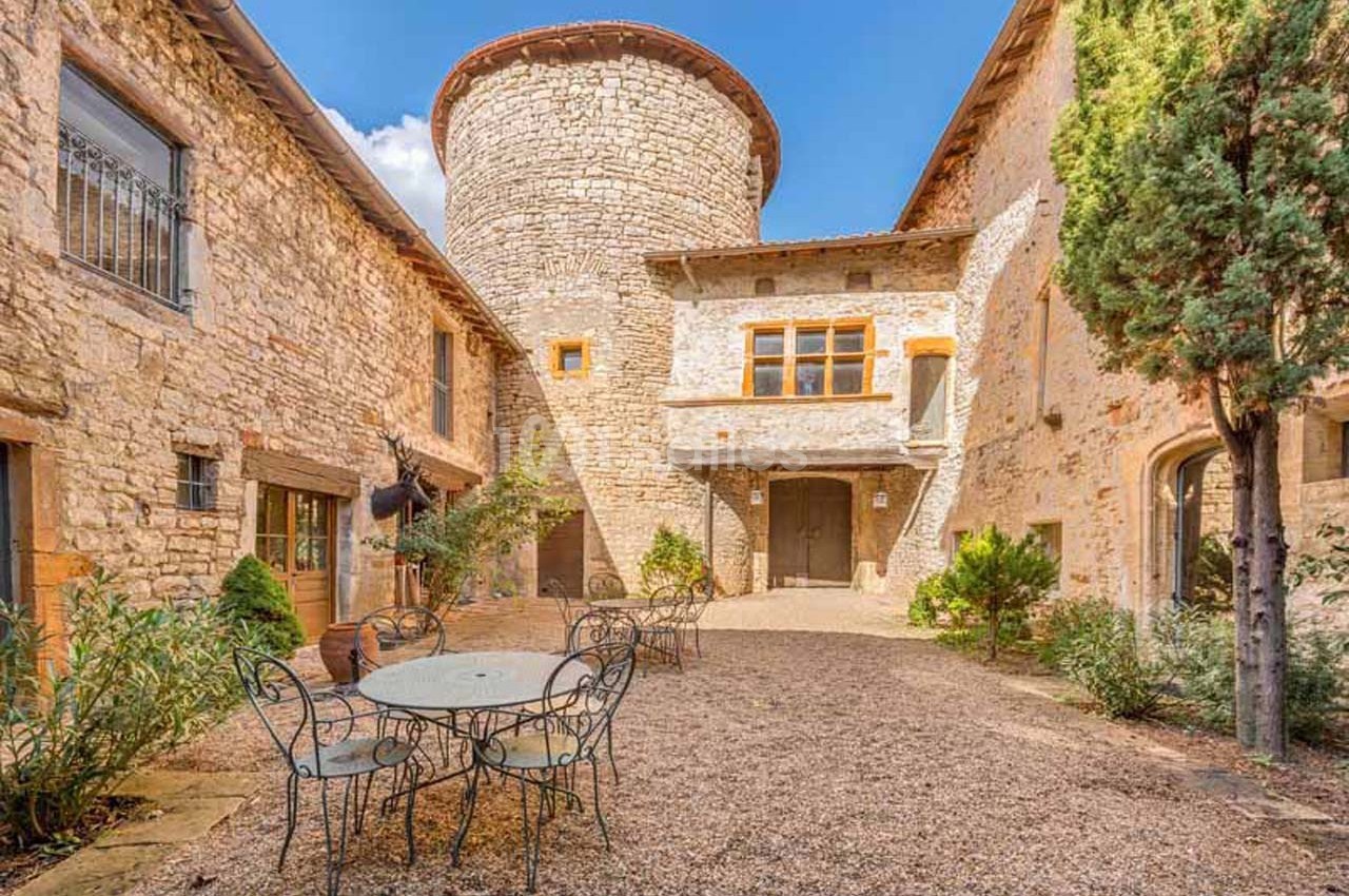 Cour intérieure d'un bâtiment en pierre avec une tour ronde, des tables en fer forgé et des plantes autour.