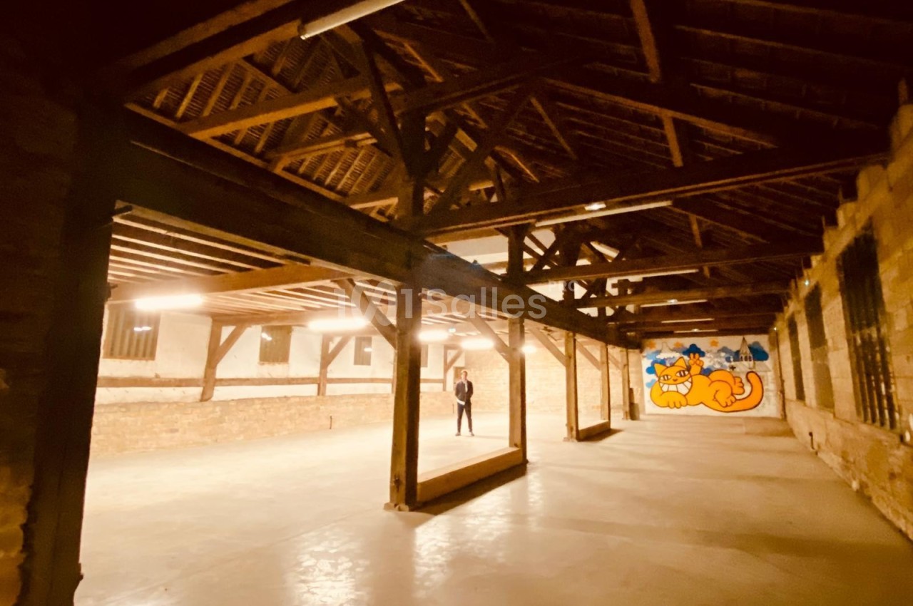 Intérieur d'un grand espace avec charpente en bois apparente, murs en briques et fresque colorée représentant un chat.
