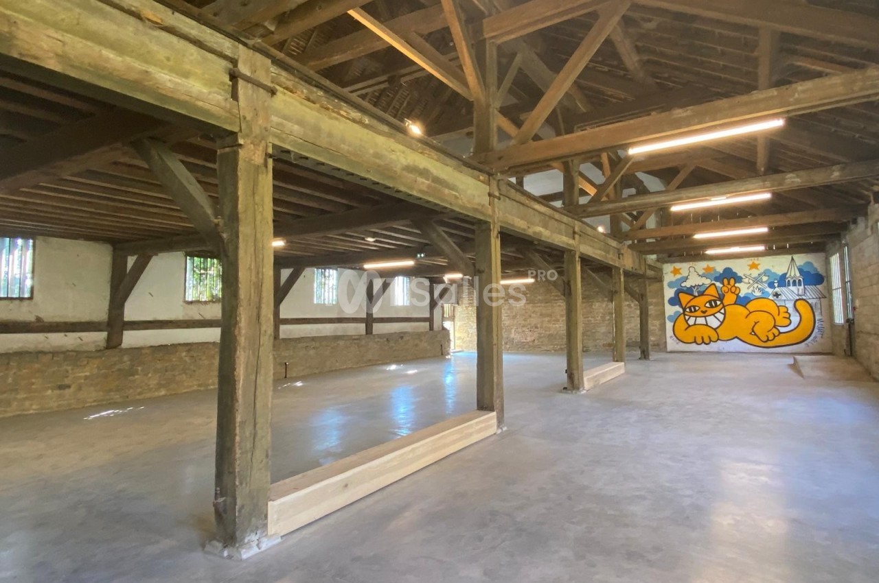 Intérieur d'un grand bâtiment en bois avec une fresque murale représentant un chat orange sur un mur au fond.