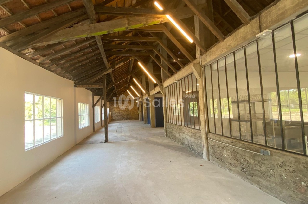 Intérieur d'un bâtiment rénové avec charpente en bois apparente, grandes fenêtres et murs en pierre et verre.
