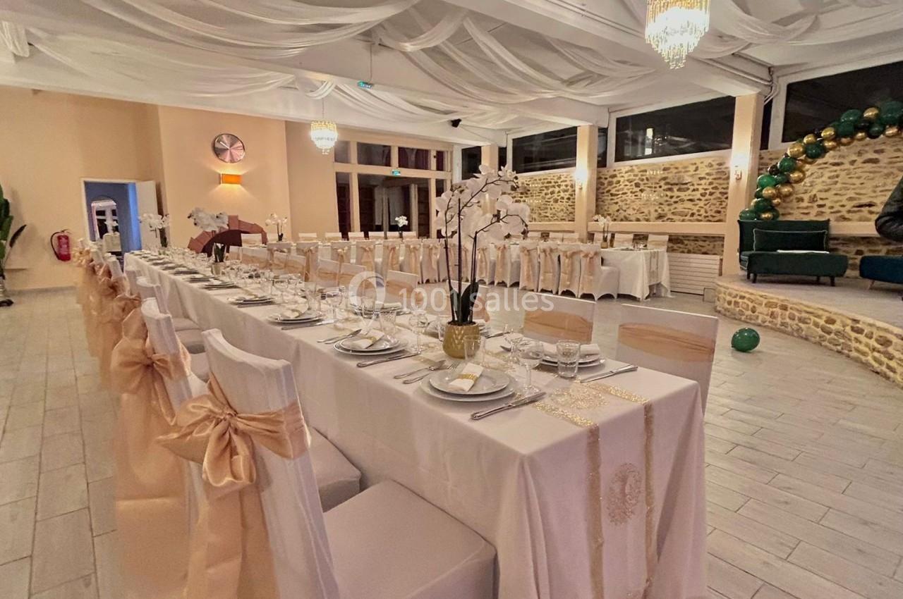 Salle de réception élégamment décorée avec des tables dressées, des chaises ornées de nœuds et un plafond drapé.